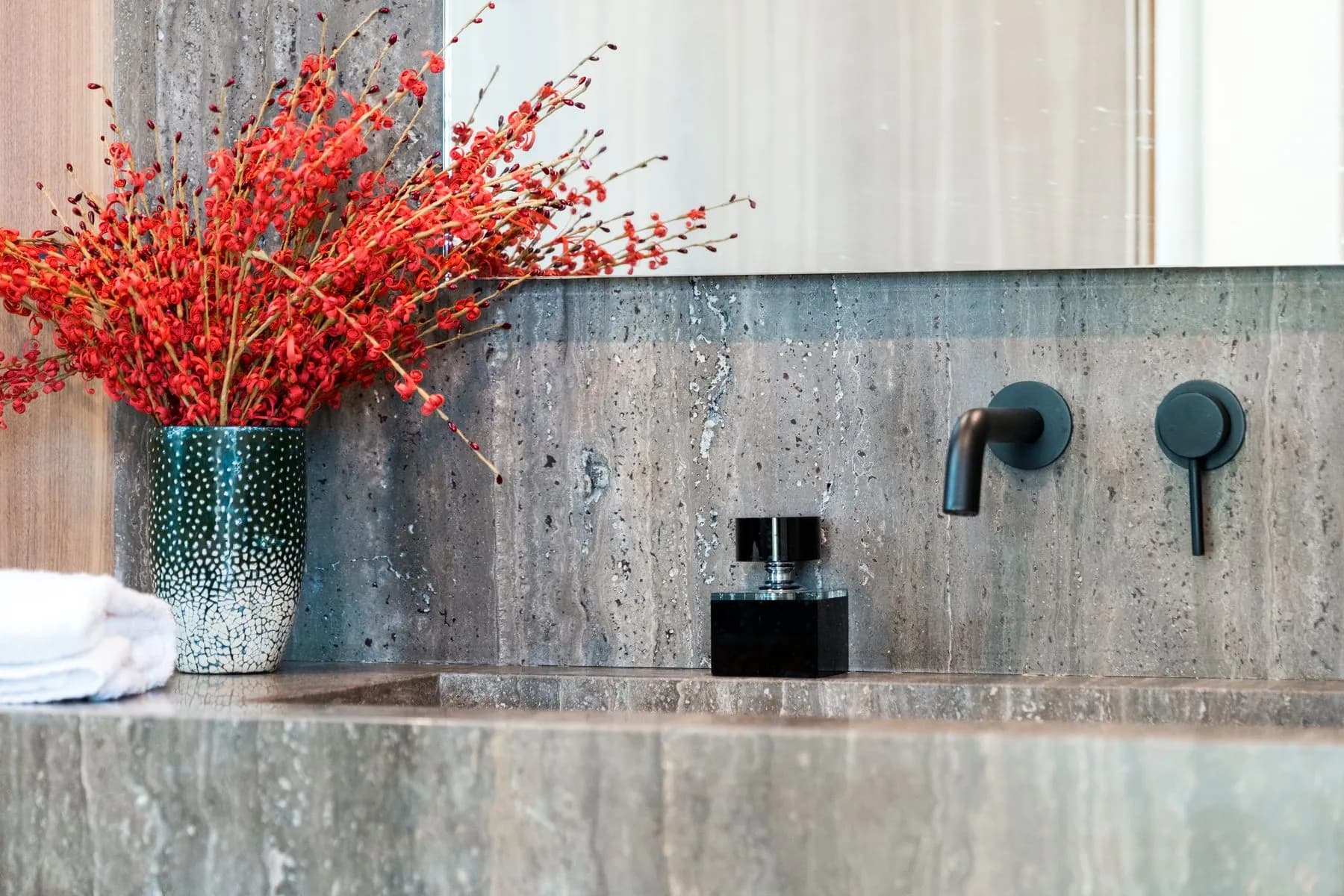 Basin cut into the stone top, with a wall-mounted matte black mixer and no visible cabinet hardware