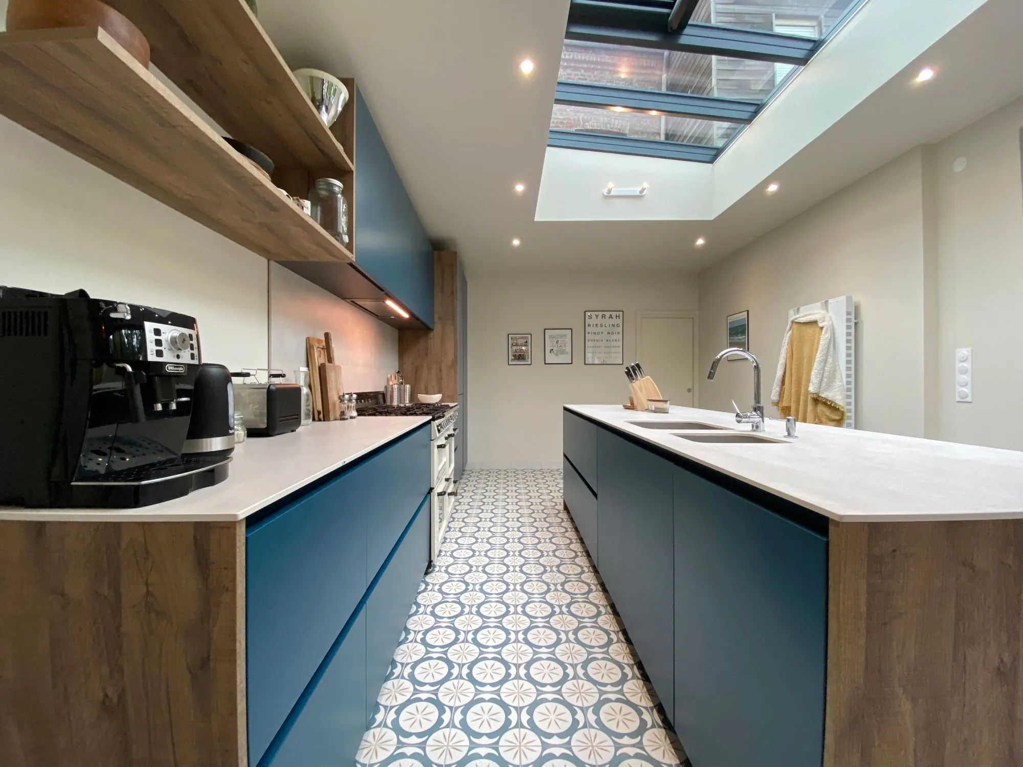 A narrow galley in blue slab fronts under a rooflight, over patterned encaustic tile