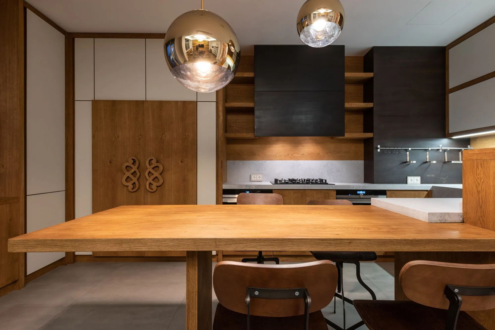 Handleless kitchen in oak and matte cream, with tall units carried to the ceiling and open oak shelving beside a black hood