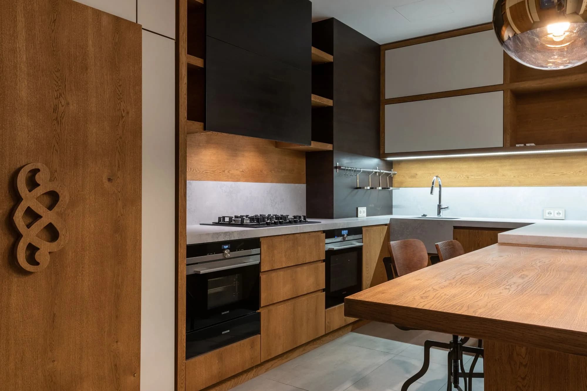 Renovated kitchen in oak veneer with handleless drawers, integrated ovens and a stone counter under a black hood