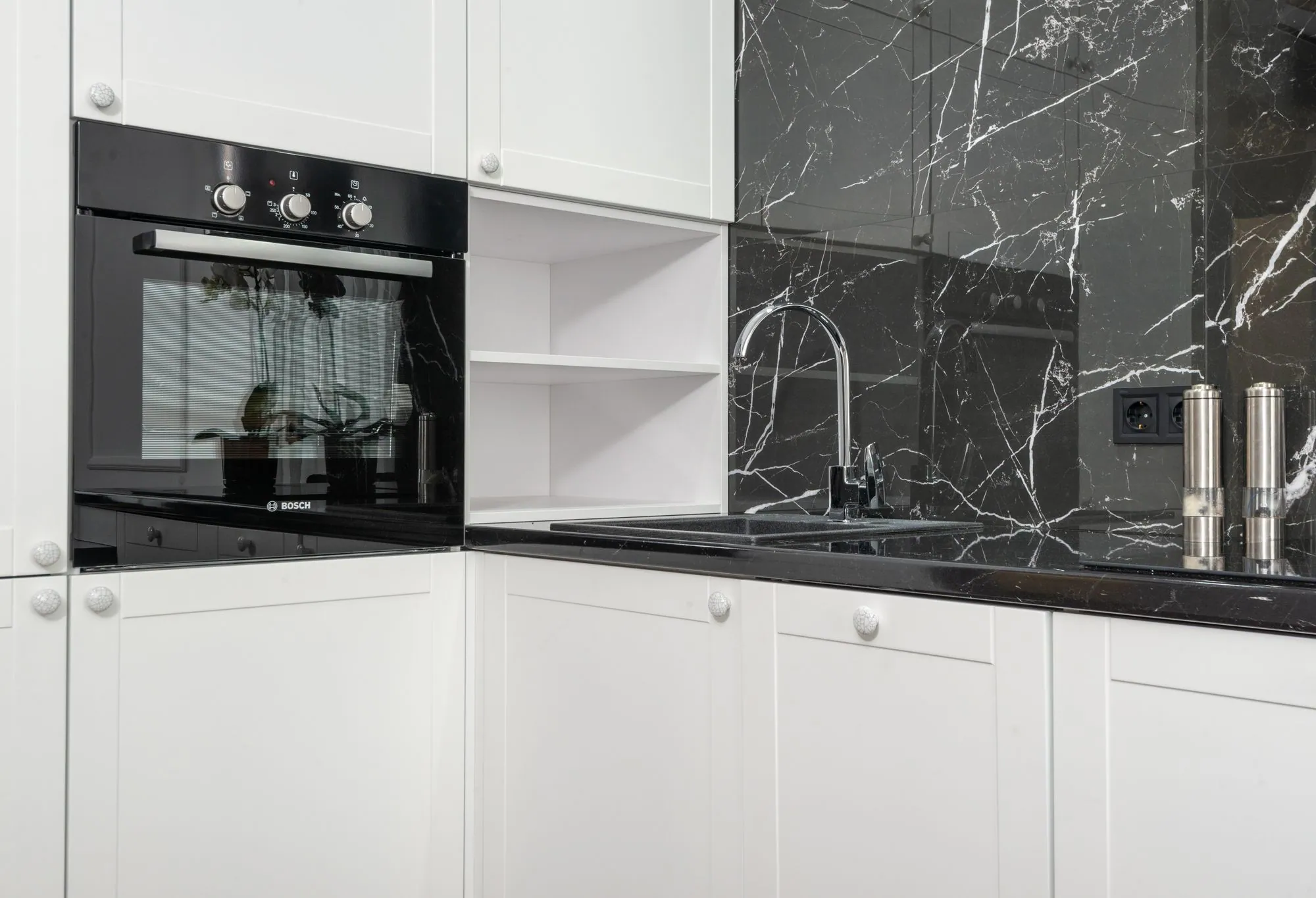 High-gloss white wall cabinets meeting a dark stone splash, lit from a window to one side