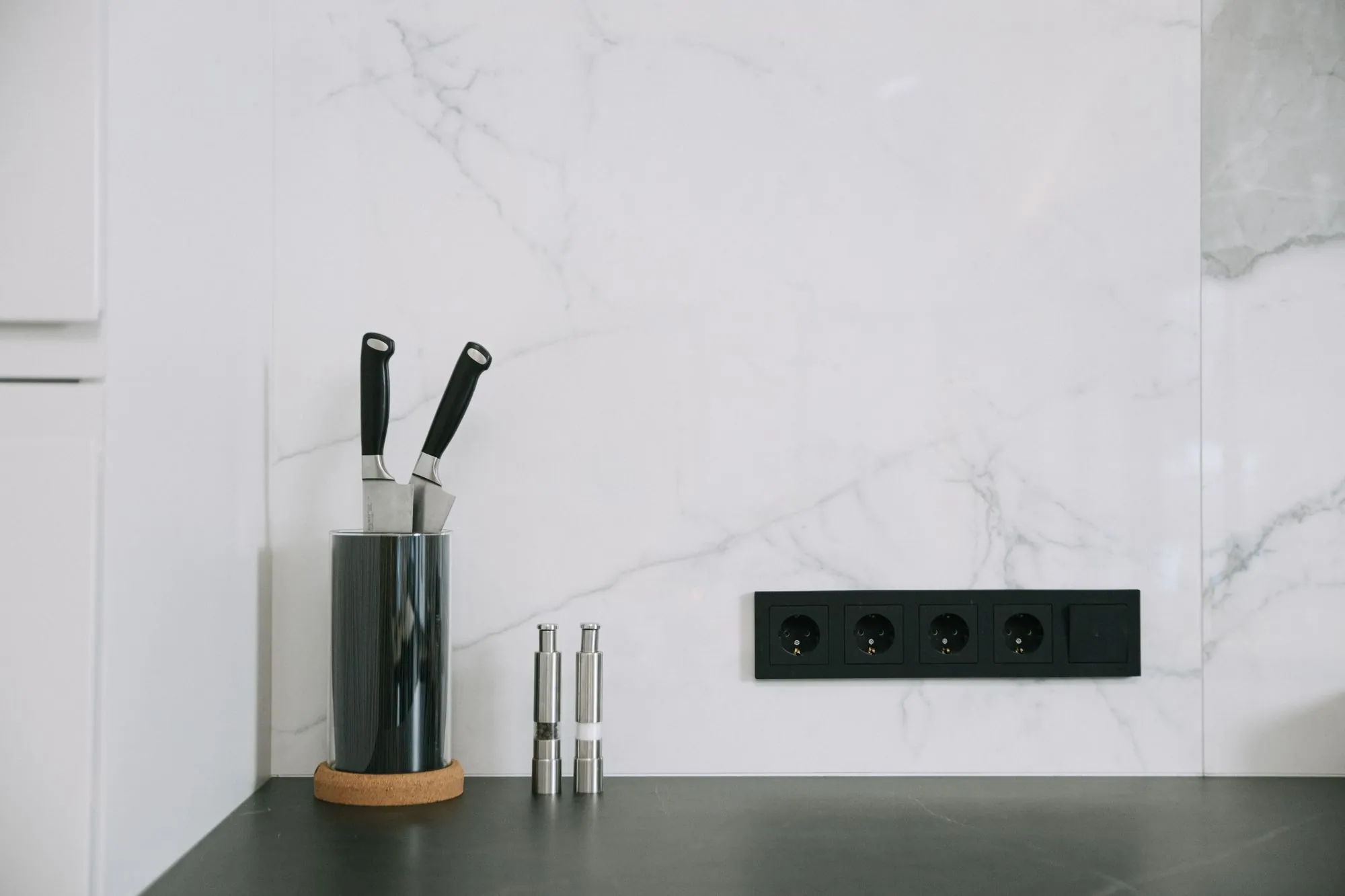 Thin dark counter meeting a marble splash, with flush black outlets set into the stone