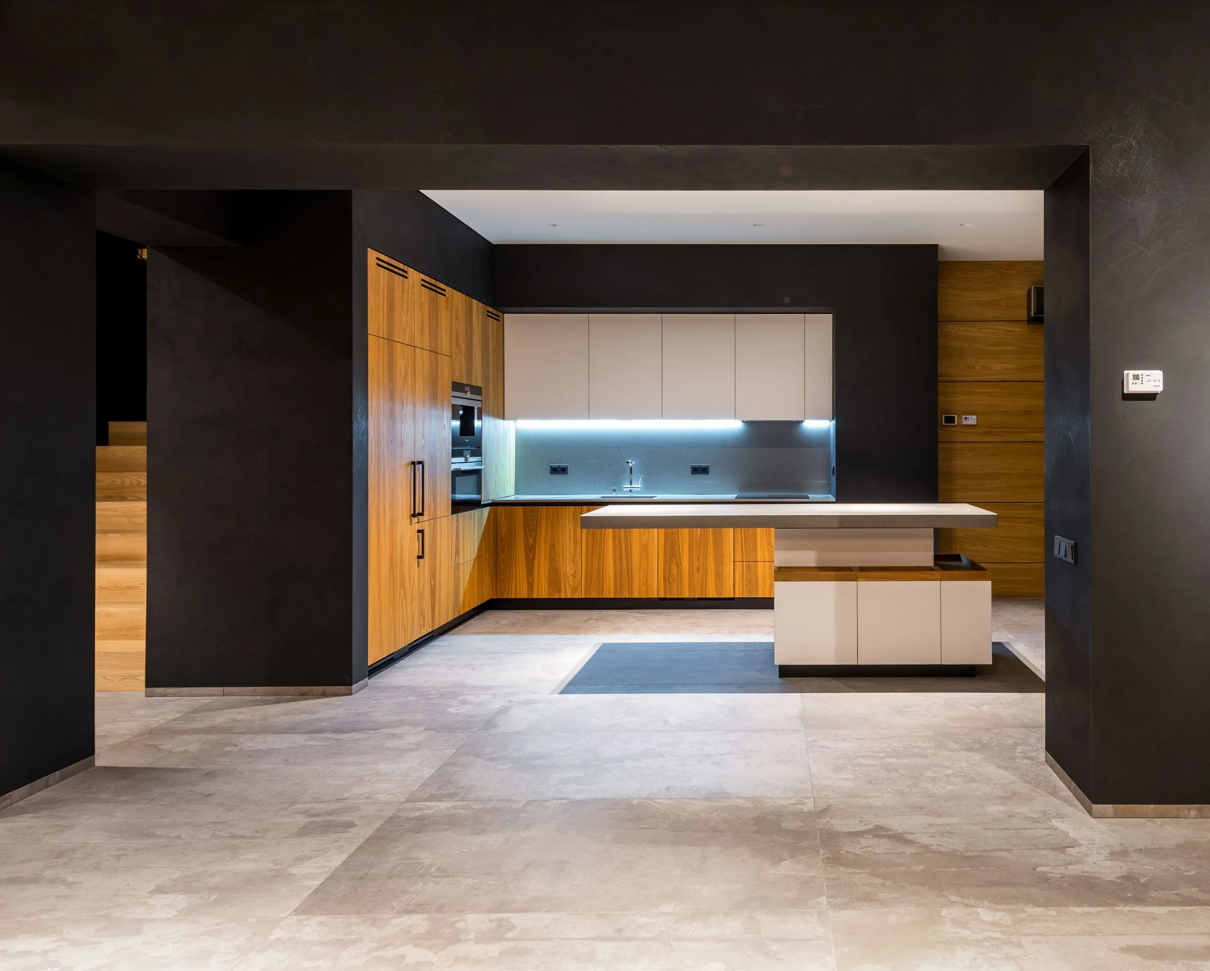 Kitchen set into an opened-up main floor, with teak veneer tall units and a cantilevered island in thin stone