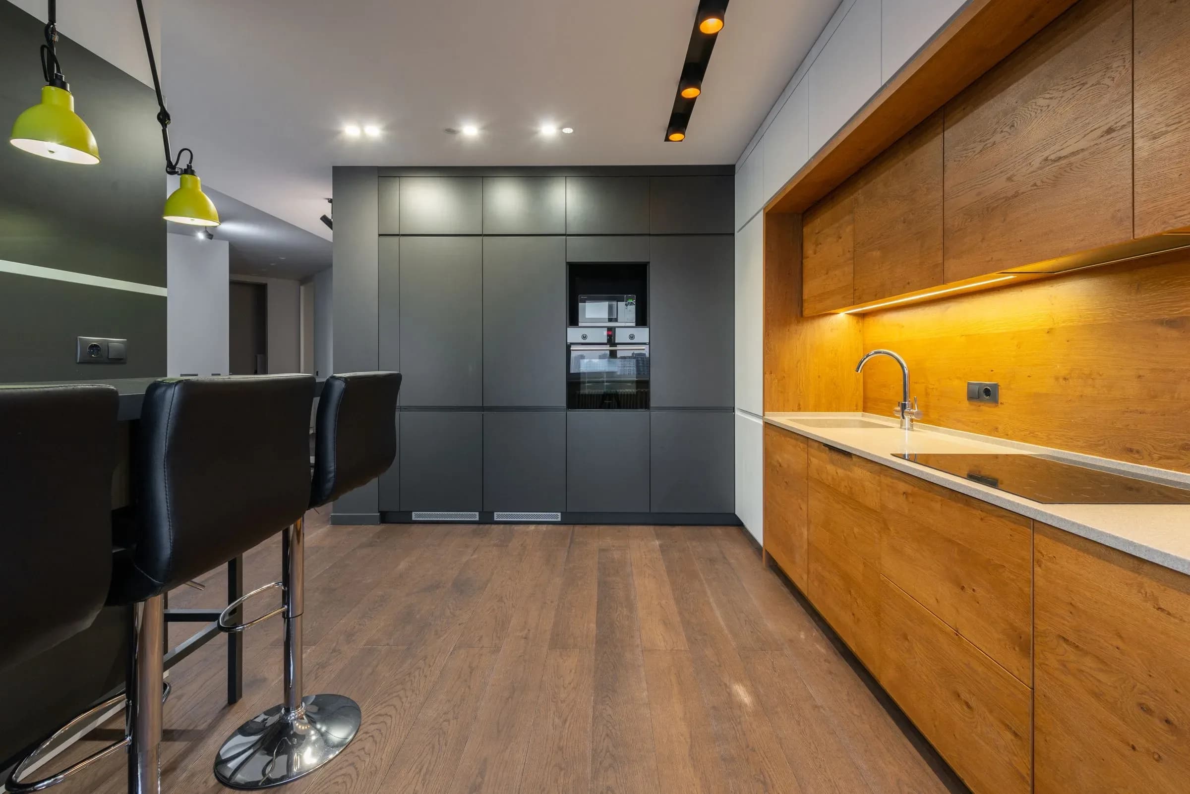 Modern kitchen with a graphite slab run down one side and a lit oak counter opposite, seen the length of the room