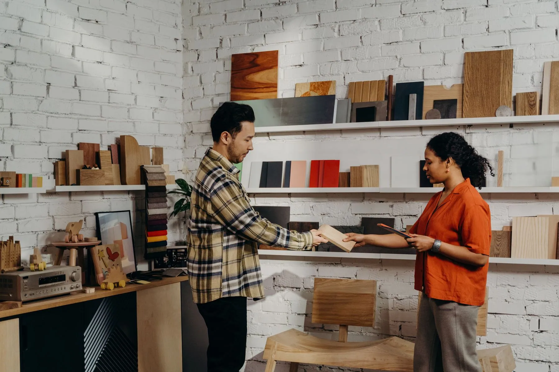 Two people comparing finish samples from a case against a wall of material boards