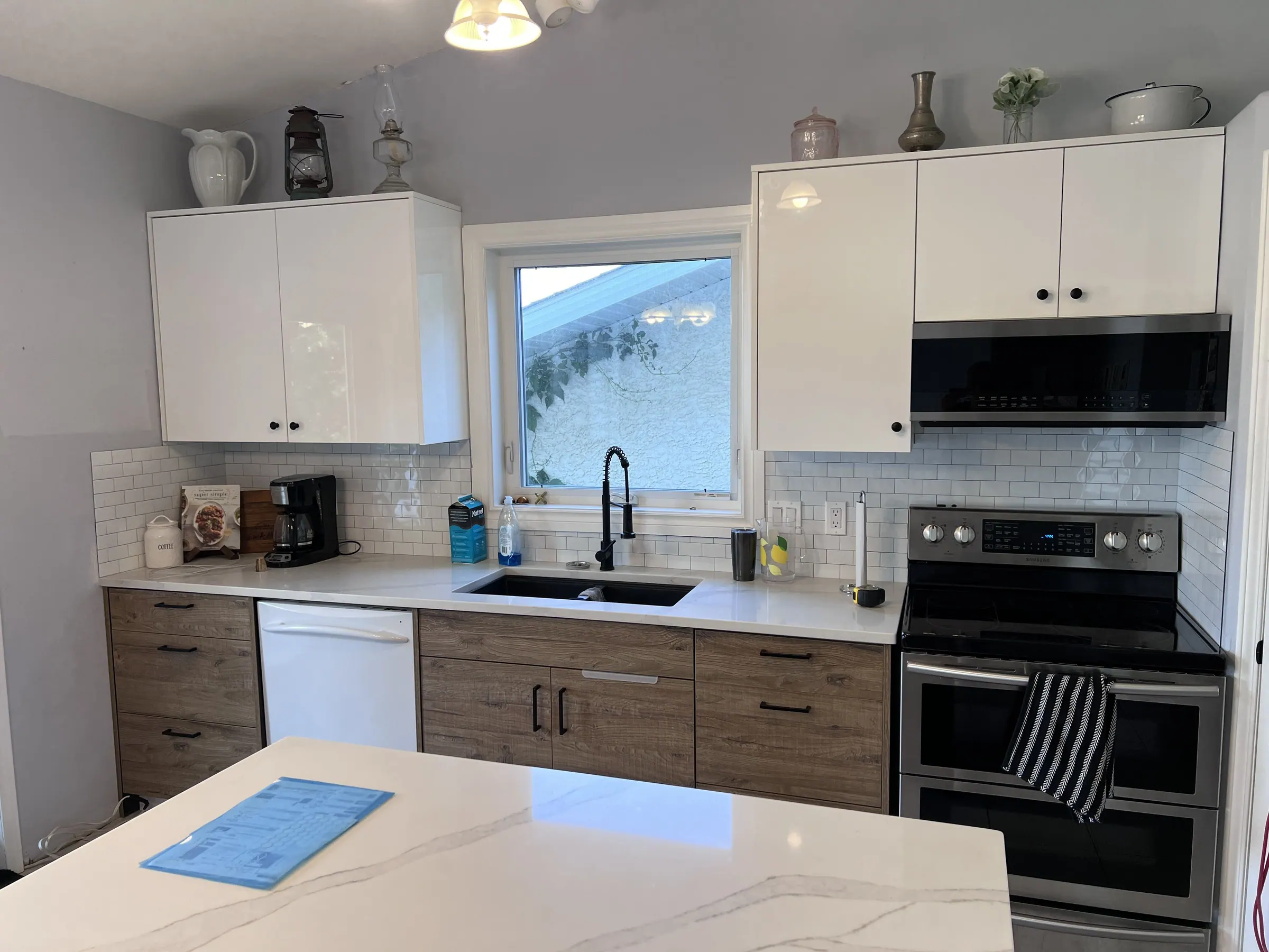 Kitchen with white wall cabinets, oak-look base units, a subway-tiled splash and a white quartz island