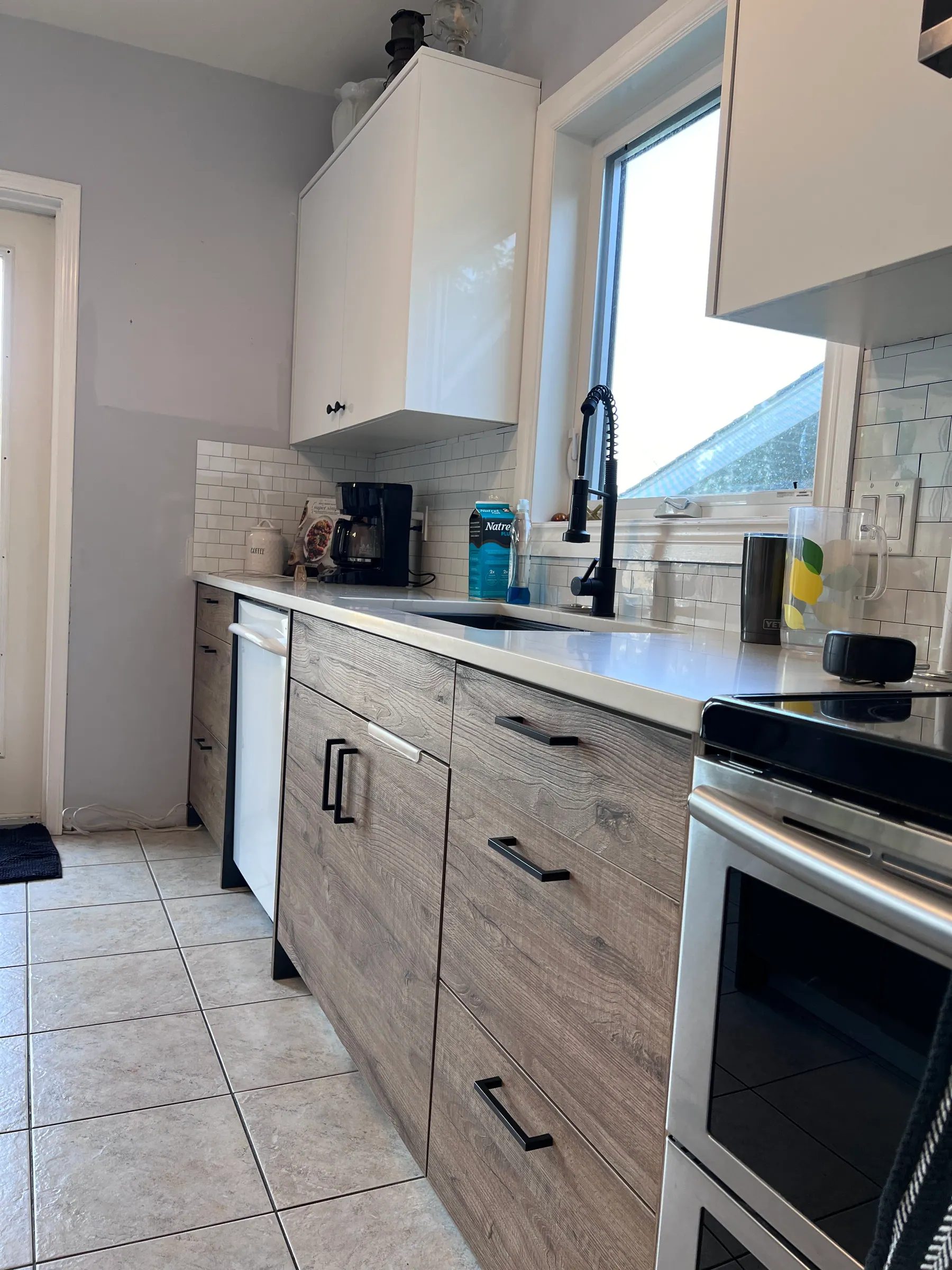 Sink run in quartz under a window, with a black tap and subway-tiled splash
