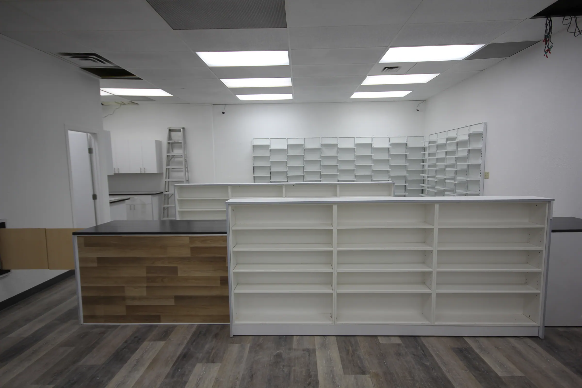 Pharmacy interior with a wood-fronted service counter, white retail shelving and dispensary benching behind