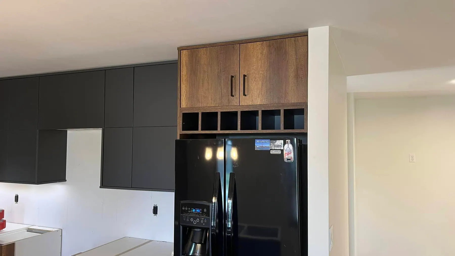 Tall storage bank in walnut-look woodgrain beside a black refrigerator, with graphite matte cabinets above
