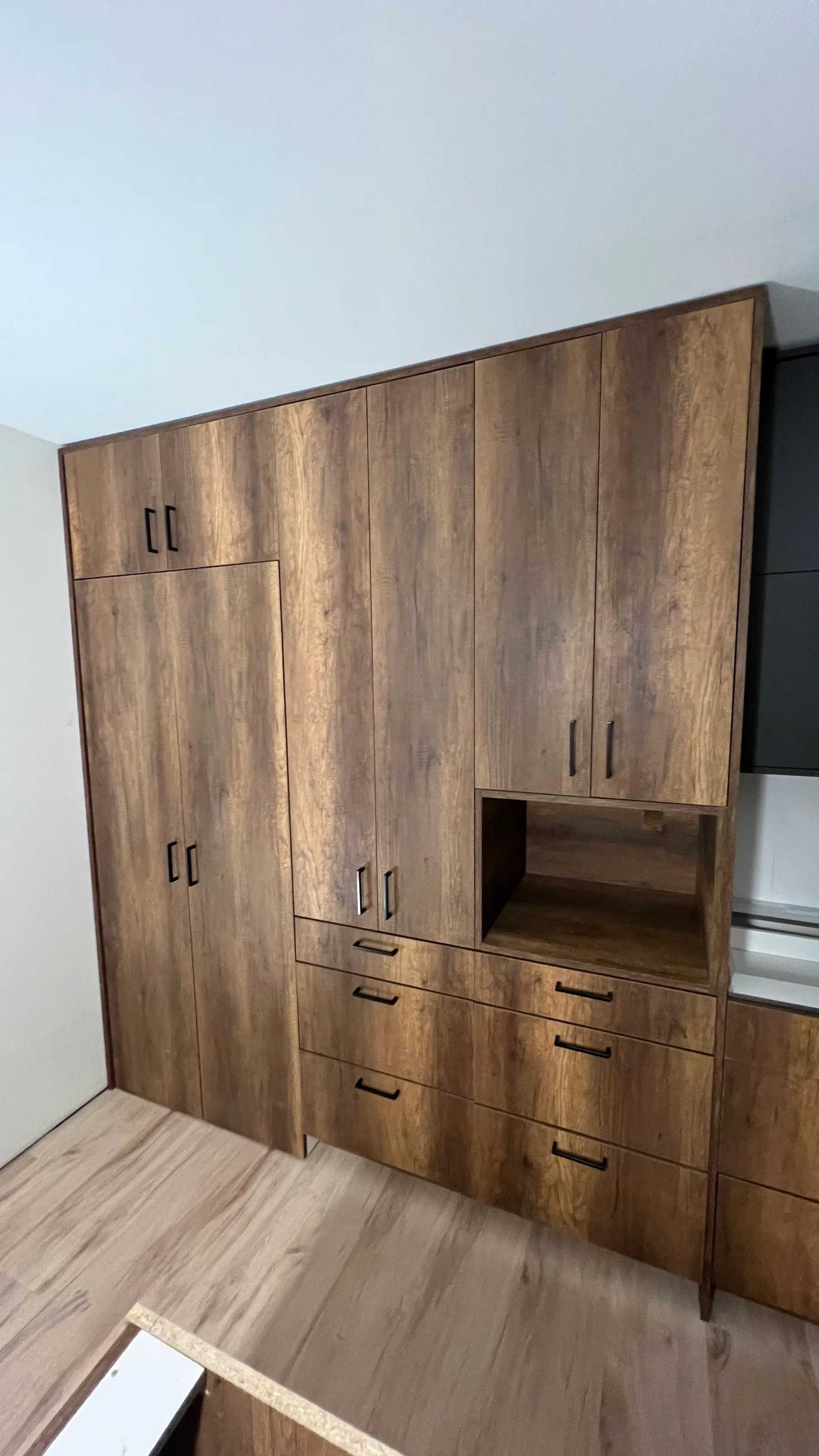 Woodgrain tall doors with vertical black bar pulls beside graphite wall cabinets
