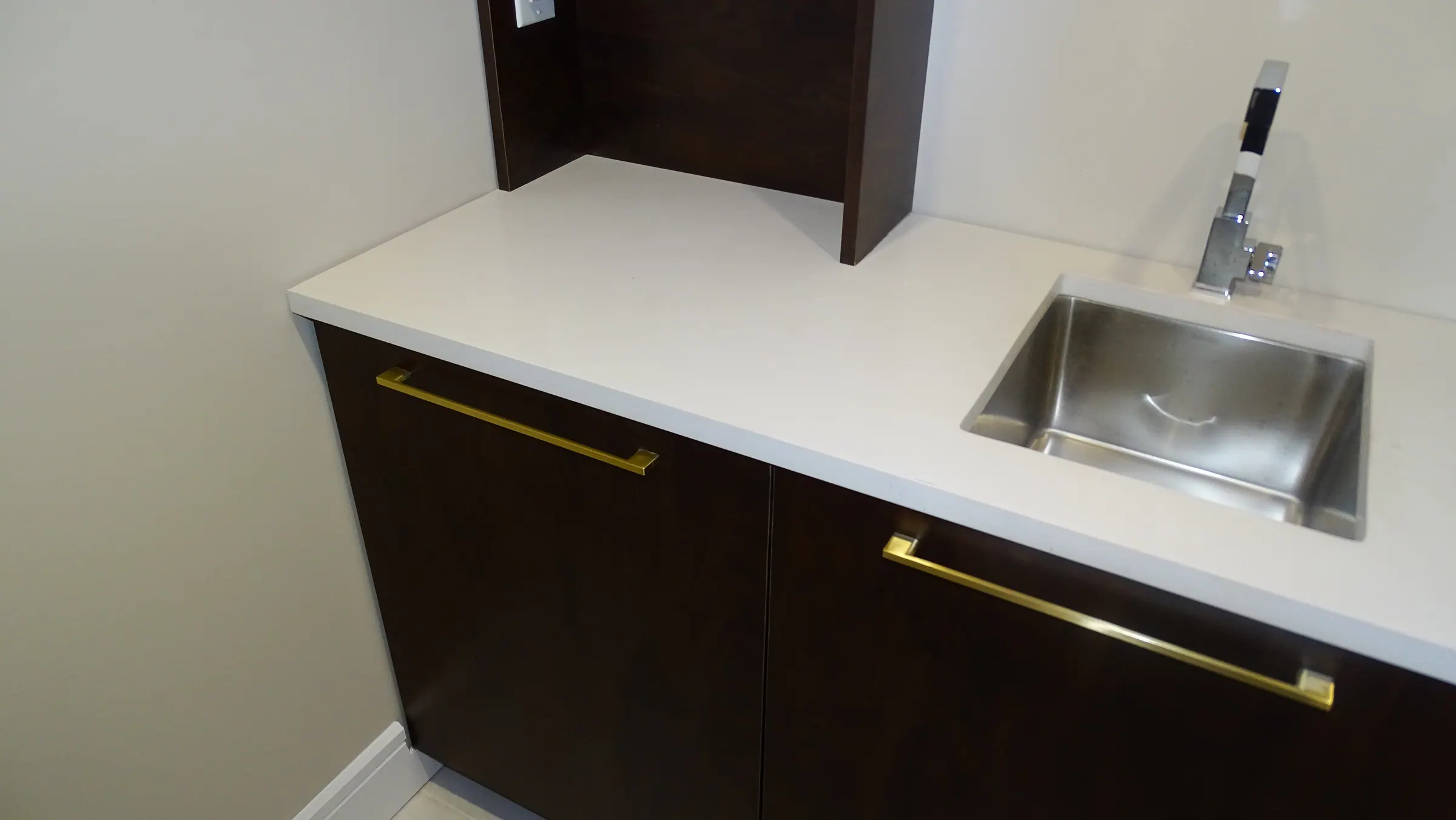 Lower-level bar in espresso cabinetry with brass pulls, a white quartz counter and an inset stainless sink