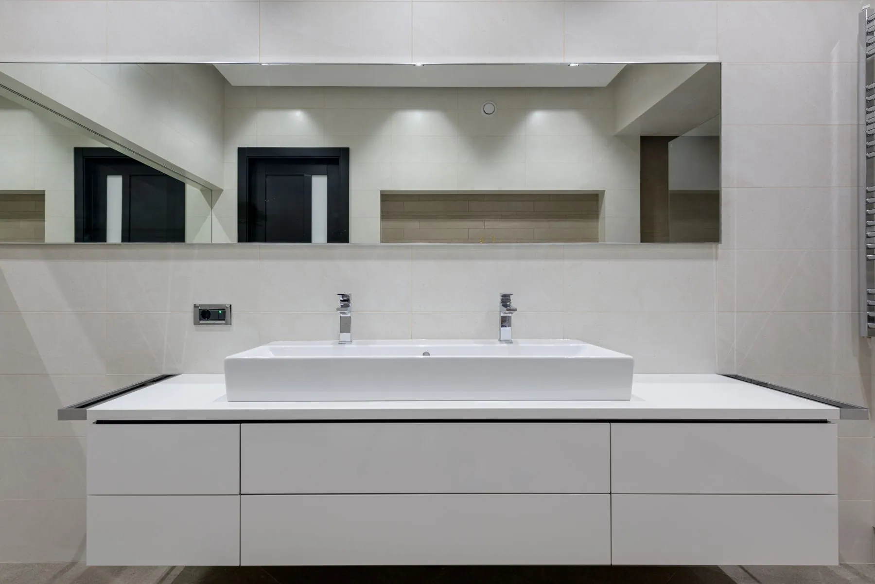Wall-hung handleless double vanity in white with a continuous slot pull and a wide trough basin