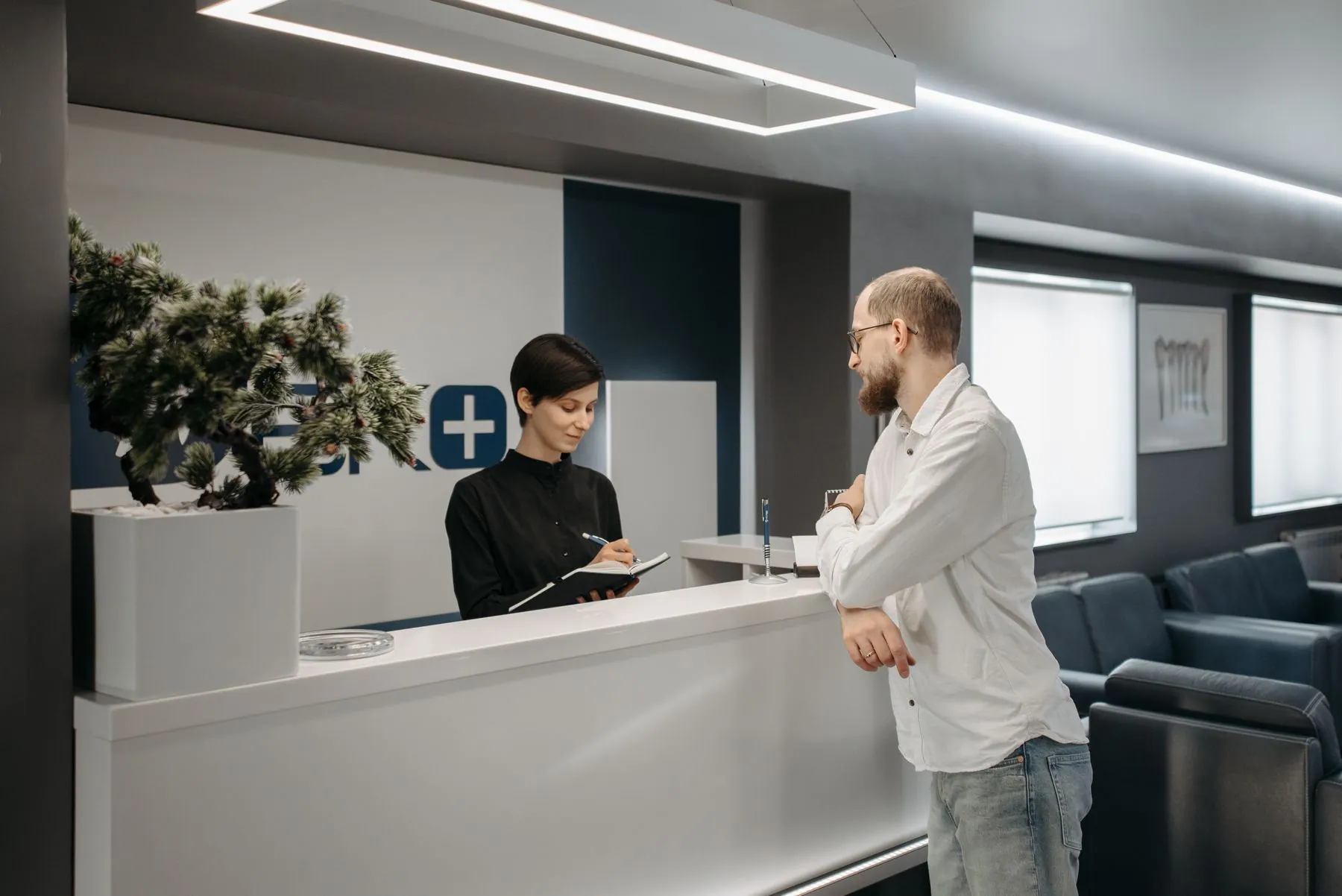 Medical clinic reception with a white solid surface counter, linear lighting and the waiting area beyond