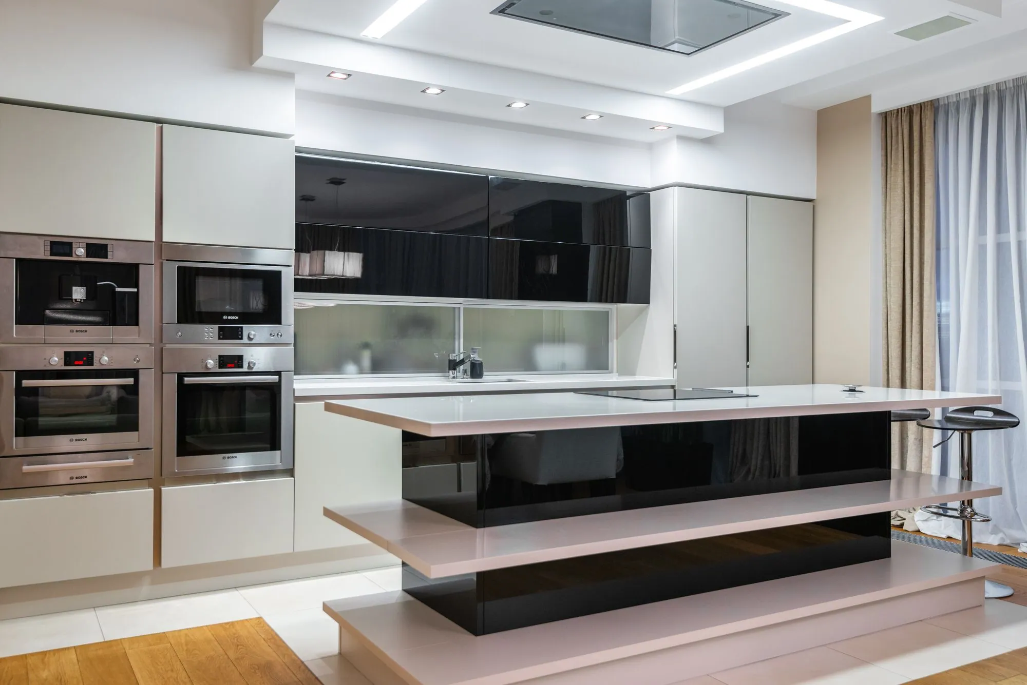 Matte cream tall banks with integrated ovens beside a gloss island and a thin white counter