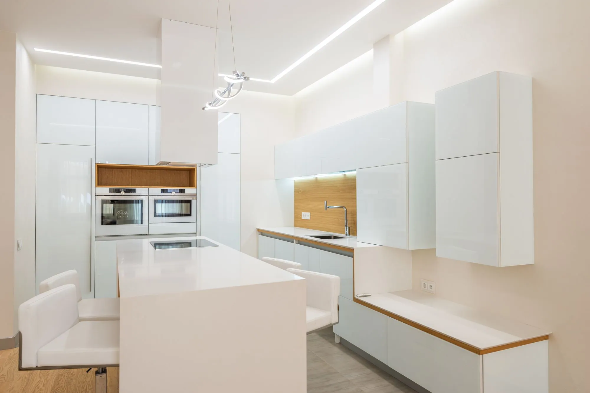 High-gloss white kitchen with oak-lined niches, integrated ovens and a thin-edged island