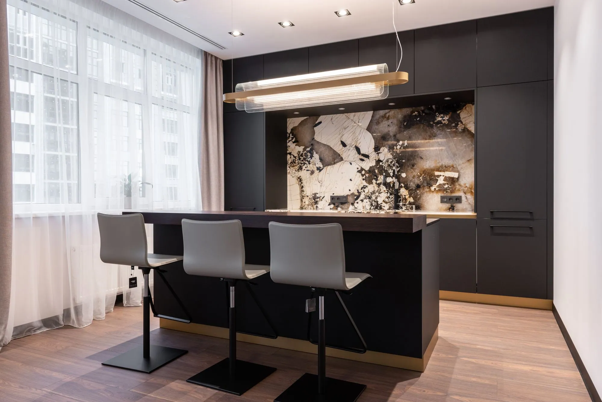 Bar run in matte black with a dark timber counter, a brass plinth line and a backlit stone panel behind the sink
