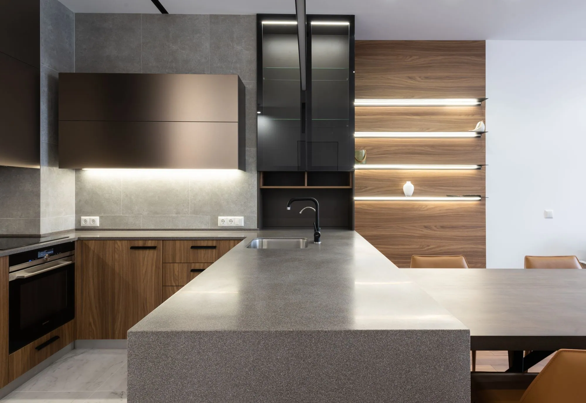 Dark handleless cabinetry meeting a timber ceiling, with a stone-topped island under concealed lighting