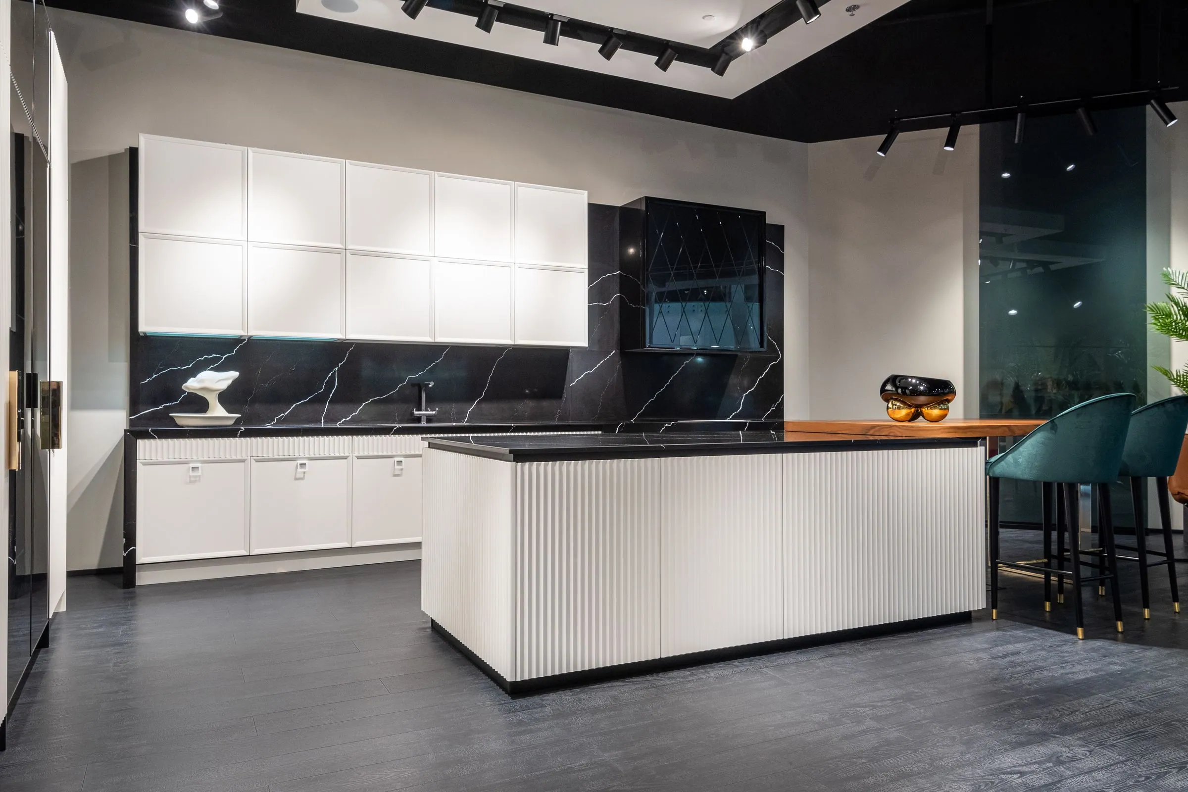 A dark handleless kitchen with an island lit from above and tall units running to the ceiling