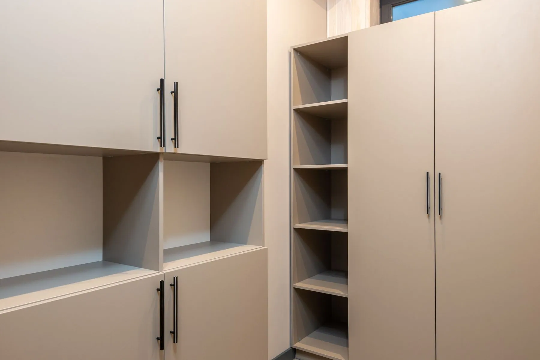 Wall-hung garage storage in slab-front laminate with slim black bar handles, open shelving and a full-height utility bank