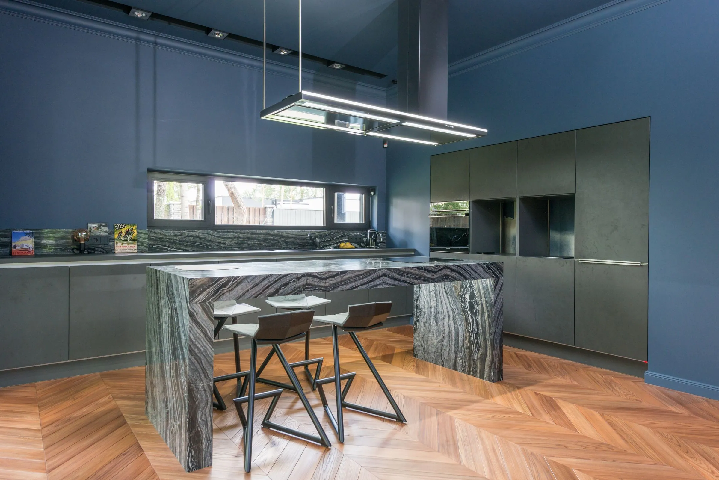 Handleless deep green slab cabinetry with a stone waterfall island and herringbone oak flooring