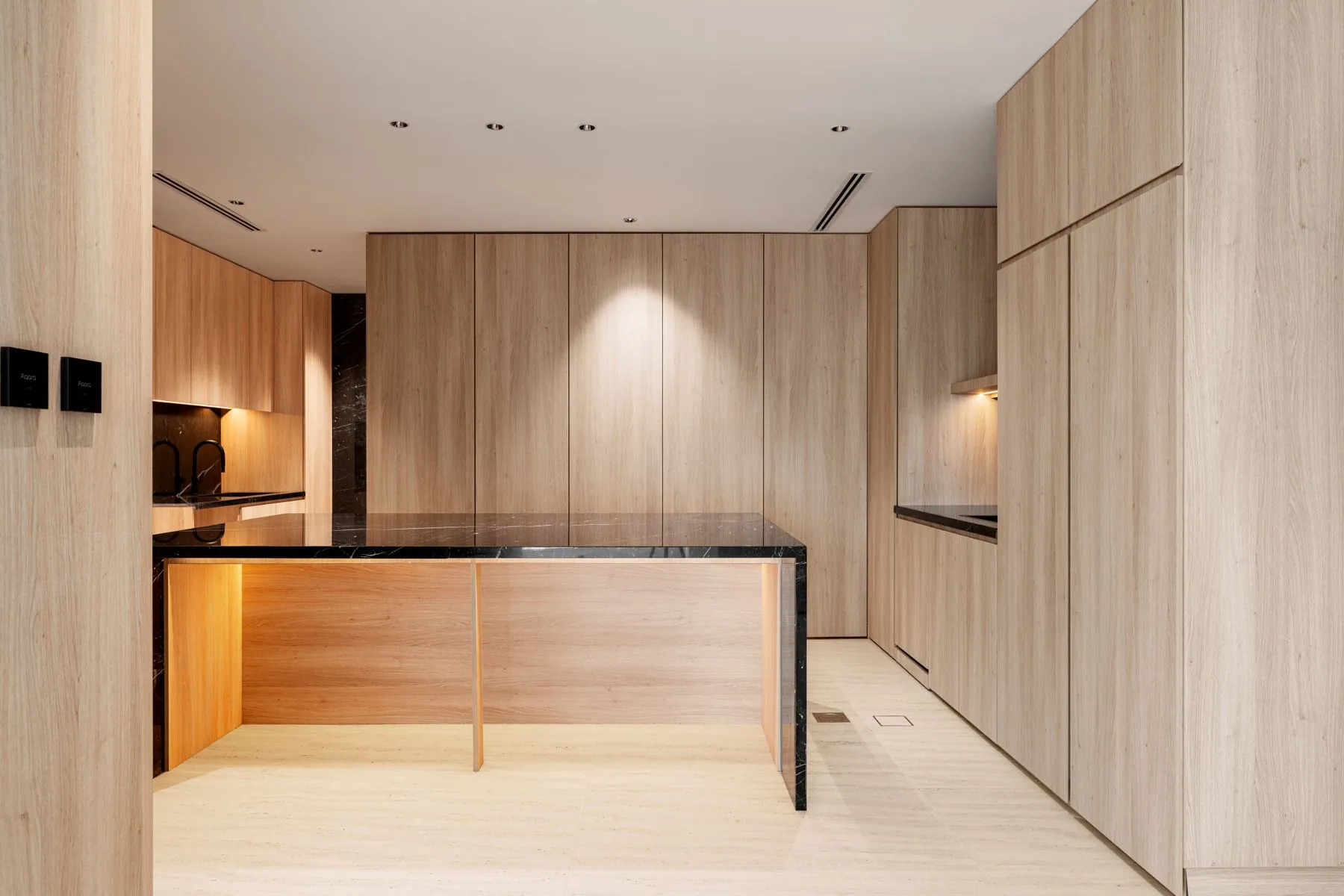 Warm oak slab cabinetry running the length of a minimal kitchen