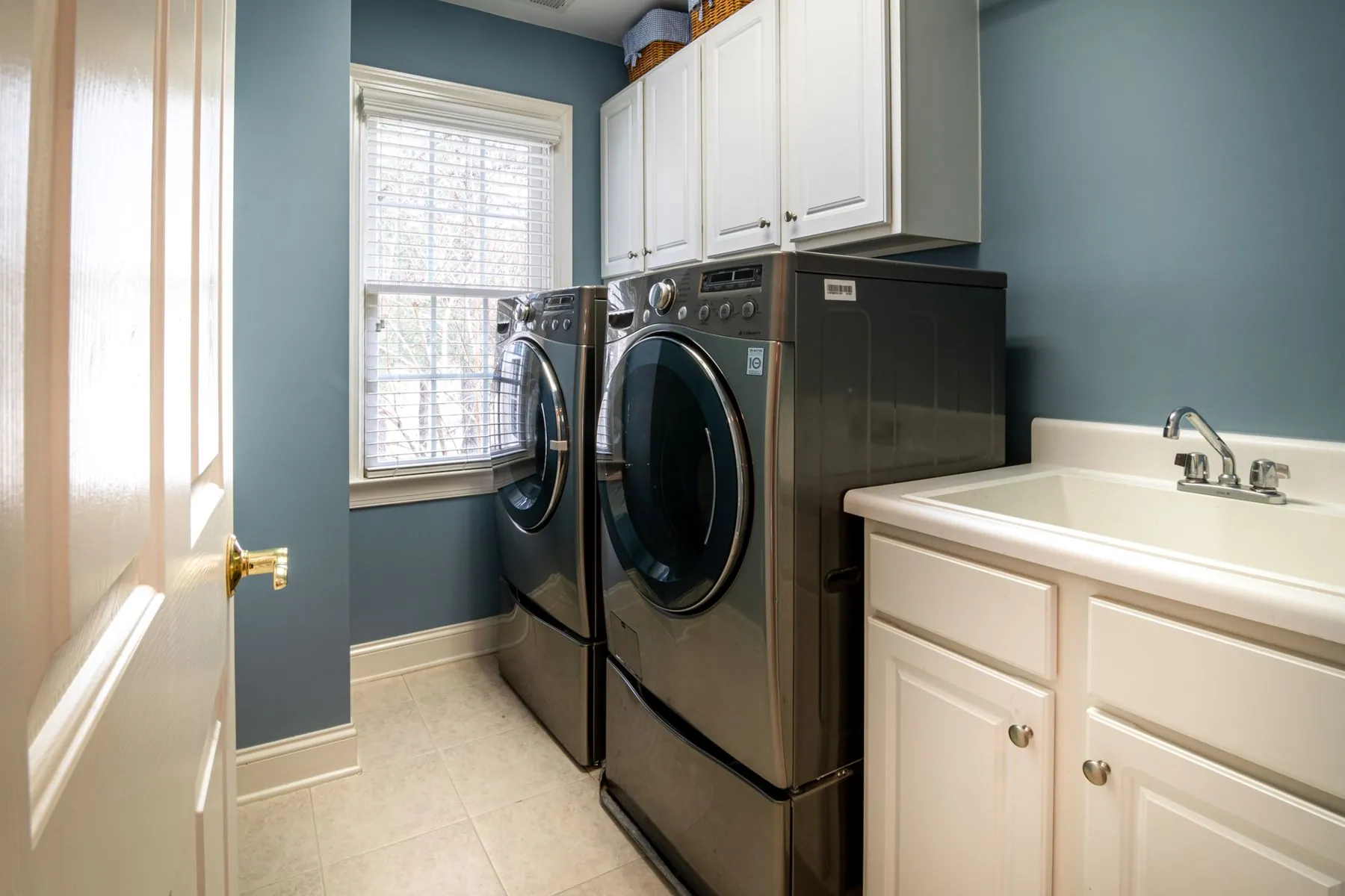 Front-loading machines on pedestals beside a base cabinet run with a utility sink