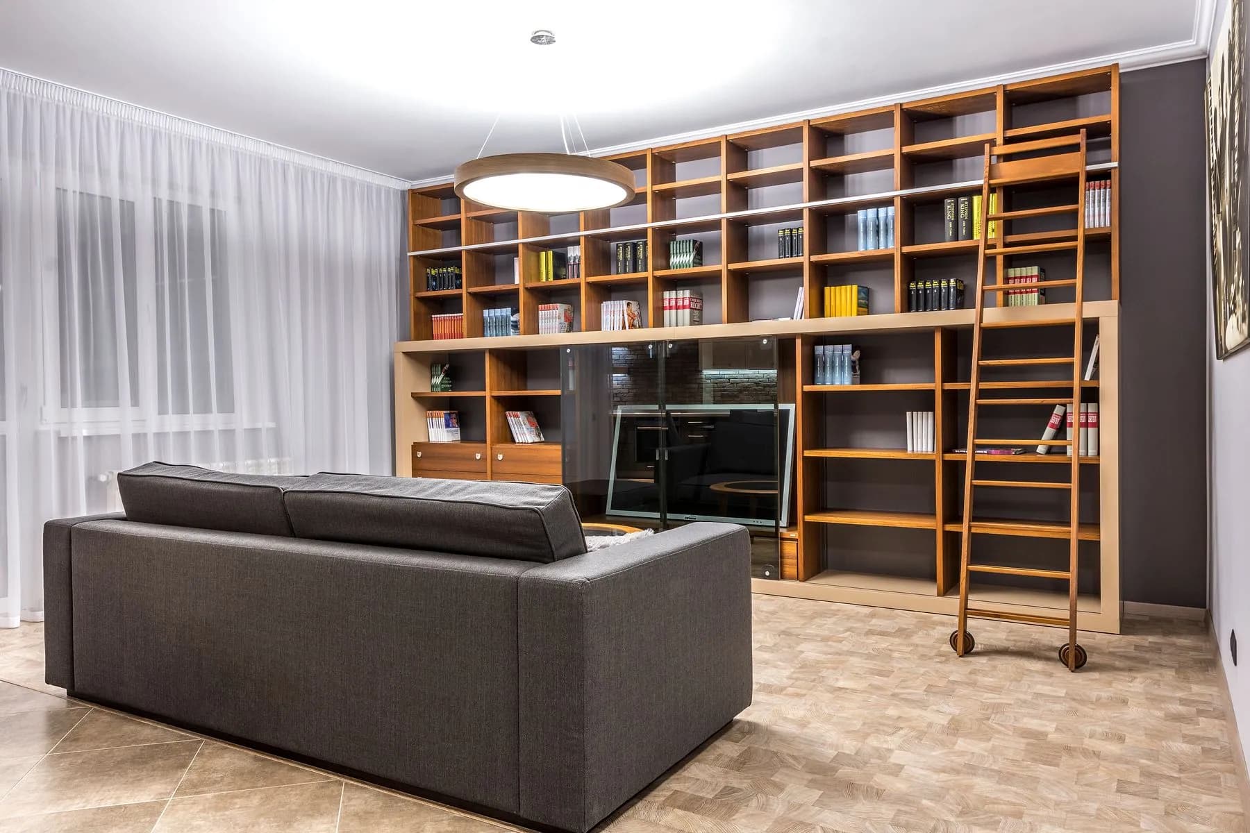 Full-height oak shelving with a rolling ladder, wrapping a living room corner