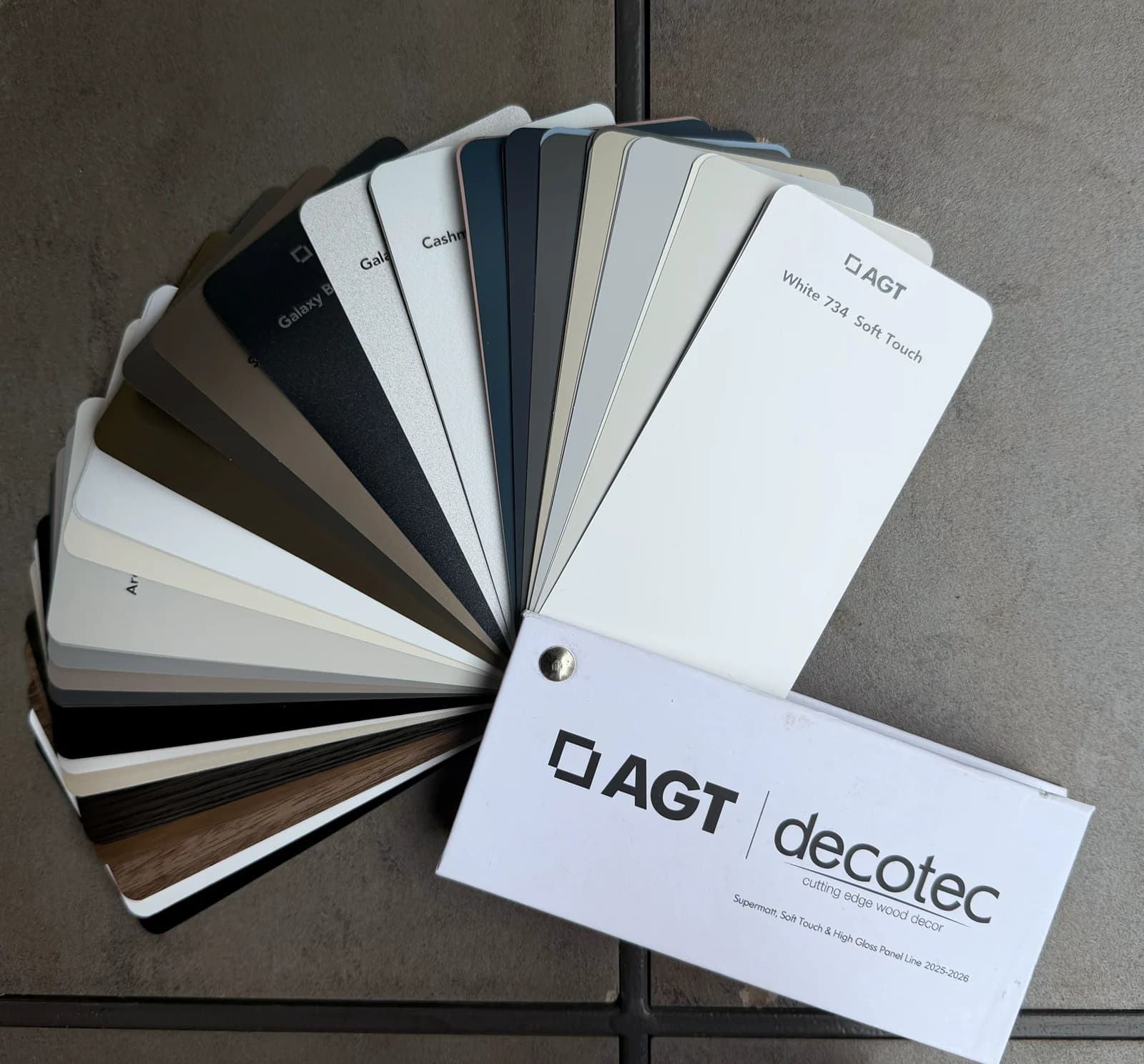 AGT decotec panel samples fanned open, showing the supermatte and soft-touch range in whites, greys, black and two woodgrains