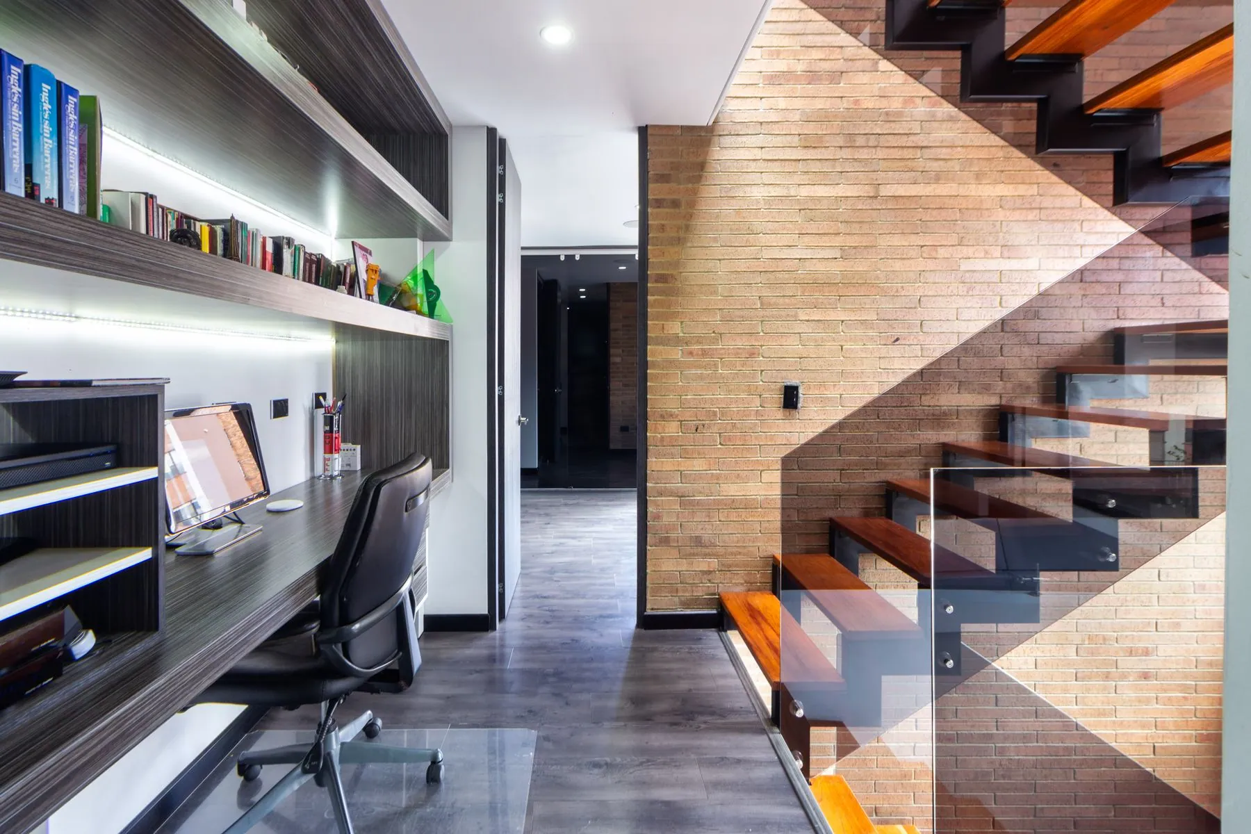 Floating desk run in a textured woodgrain melamine with LED-lit open shelving above and no visible handles