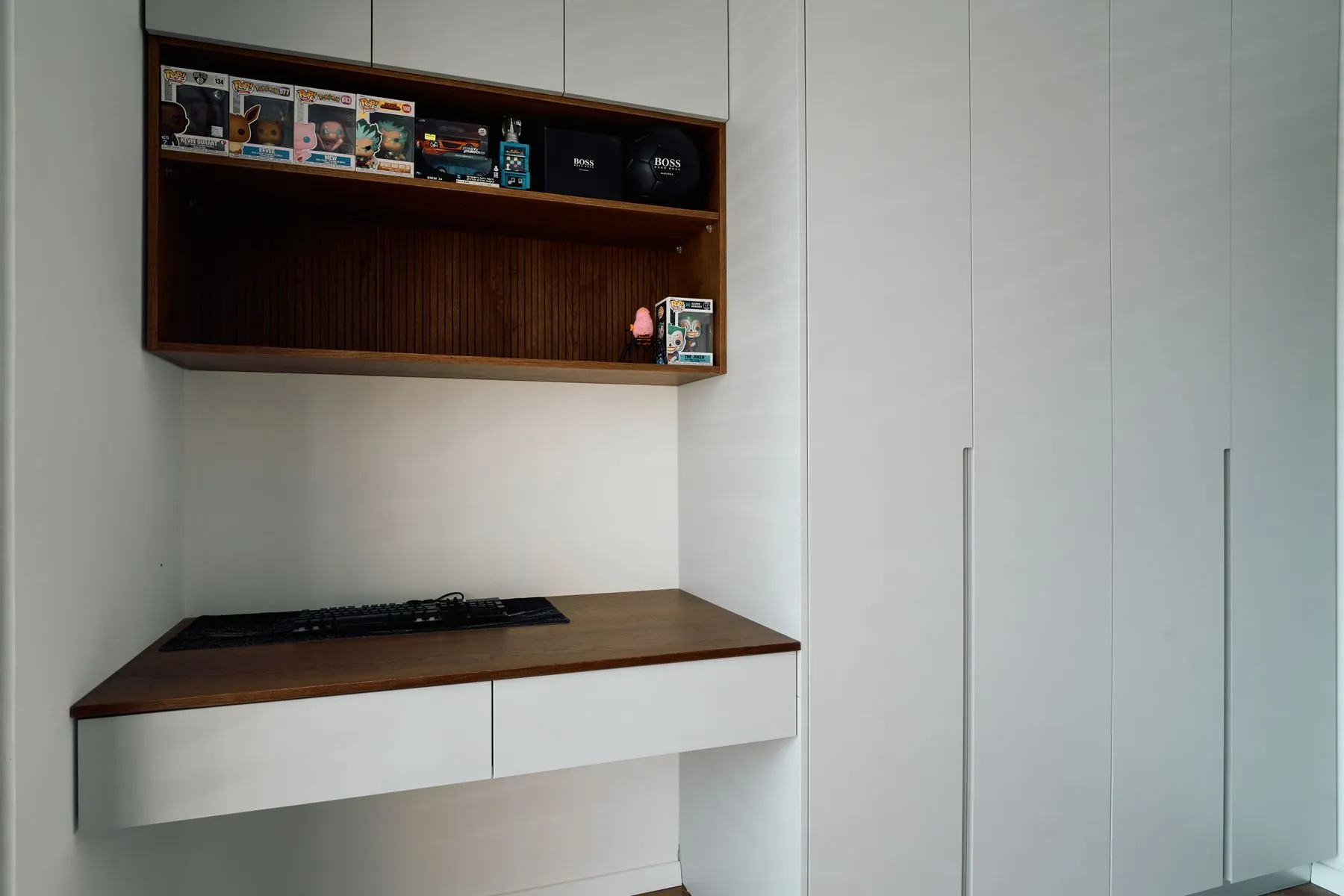 Handleless white matte tall units running floor to ceiling beside a floating desk with a walnut top and integrated finger-pull drawers