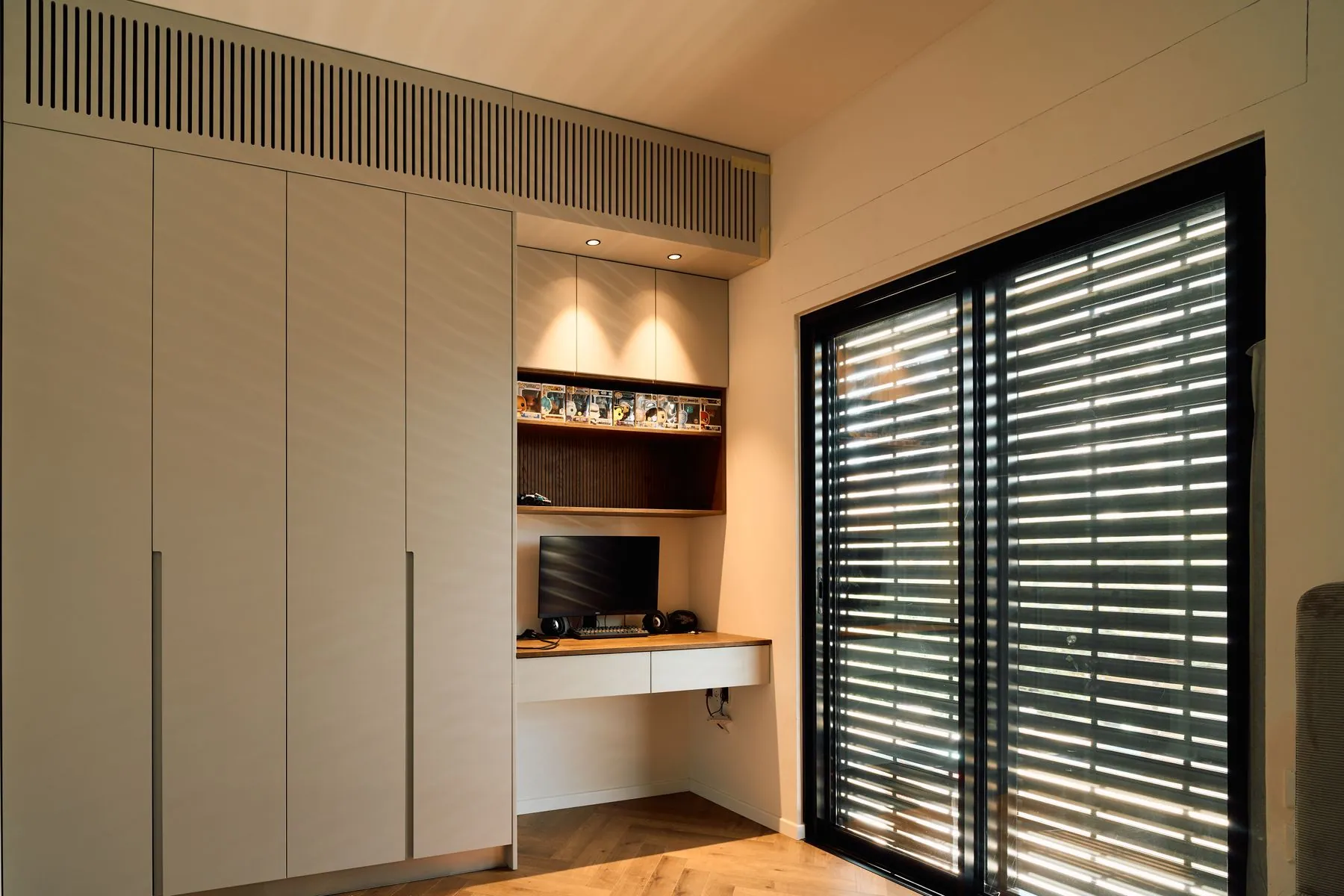 Full-height handleless storage in a warm stone colour with an integrated desk nook and a lit display shelf
