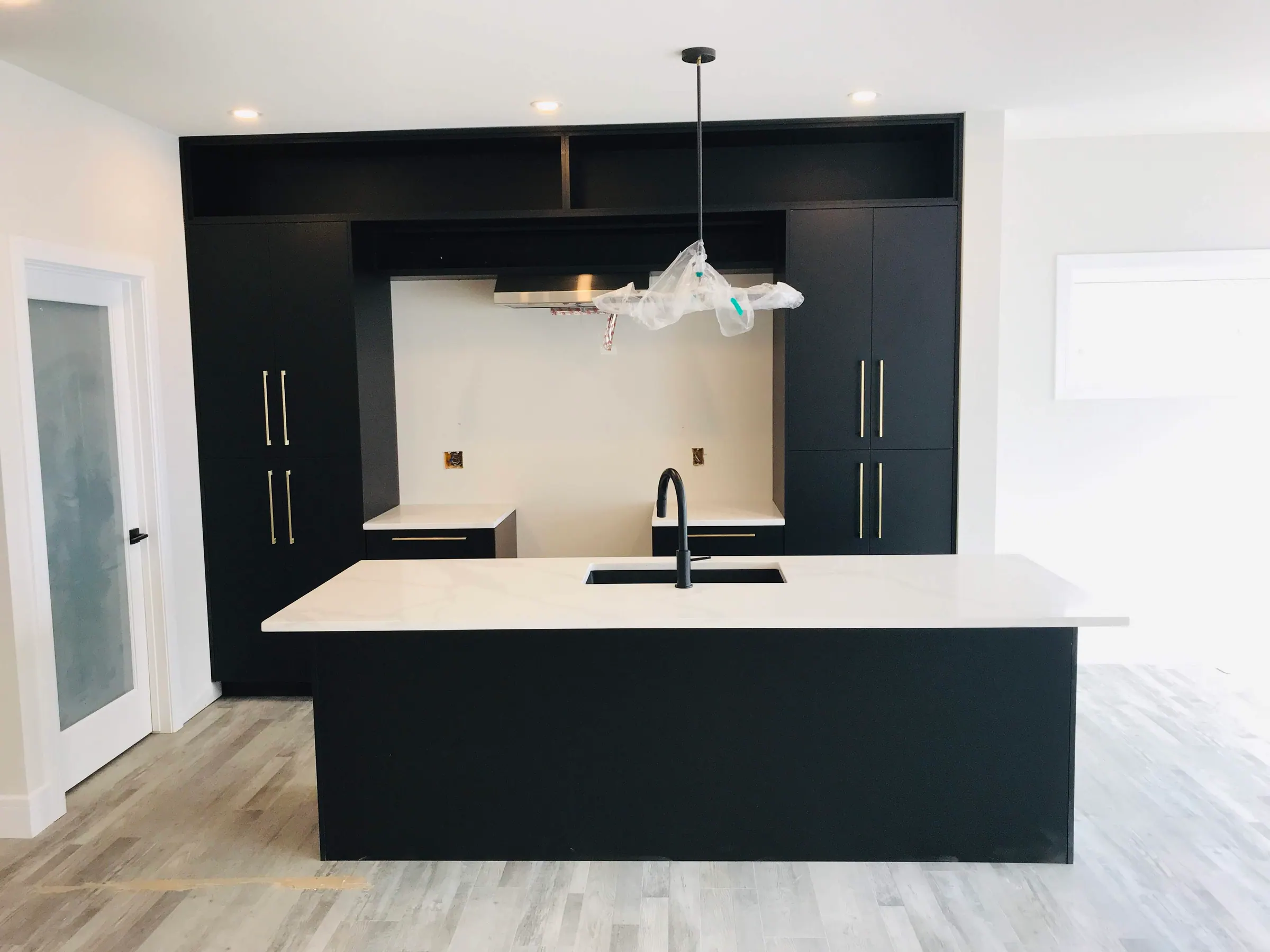 Matte black kitchen with brass bar pulls, a white quartz island and black tall units behind