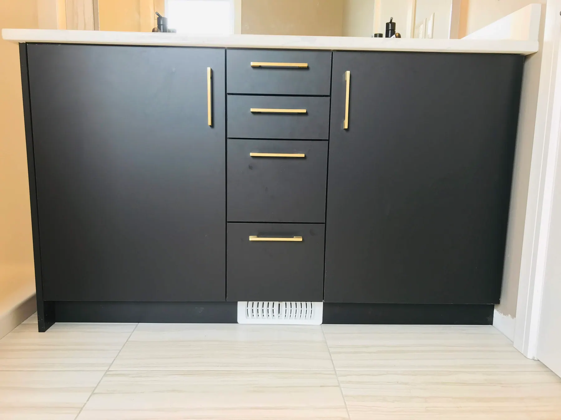 Bathroom vanity in matte black with brass pulls and a quartz top