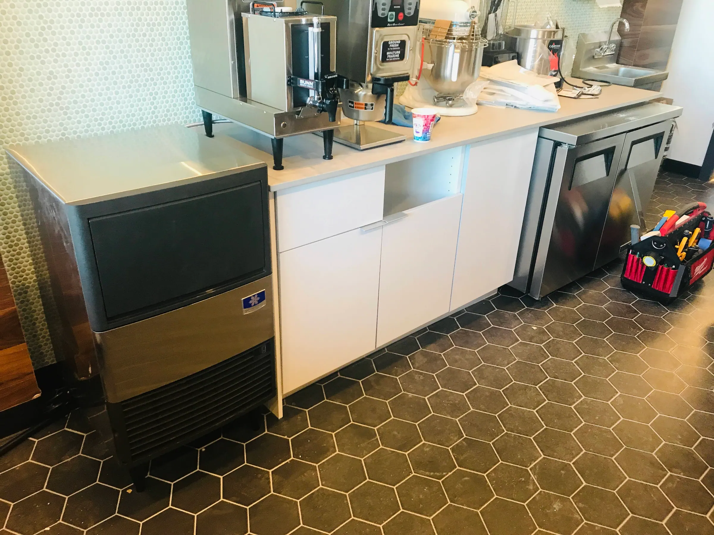 Donut shop service area with white slab counters, stainless equipment and a hexagonal tiled floor