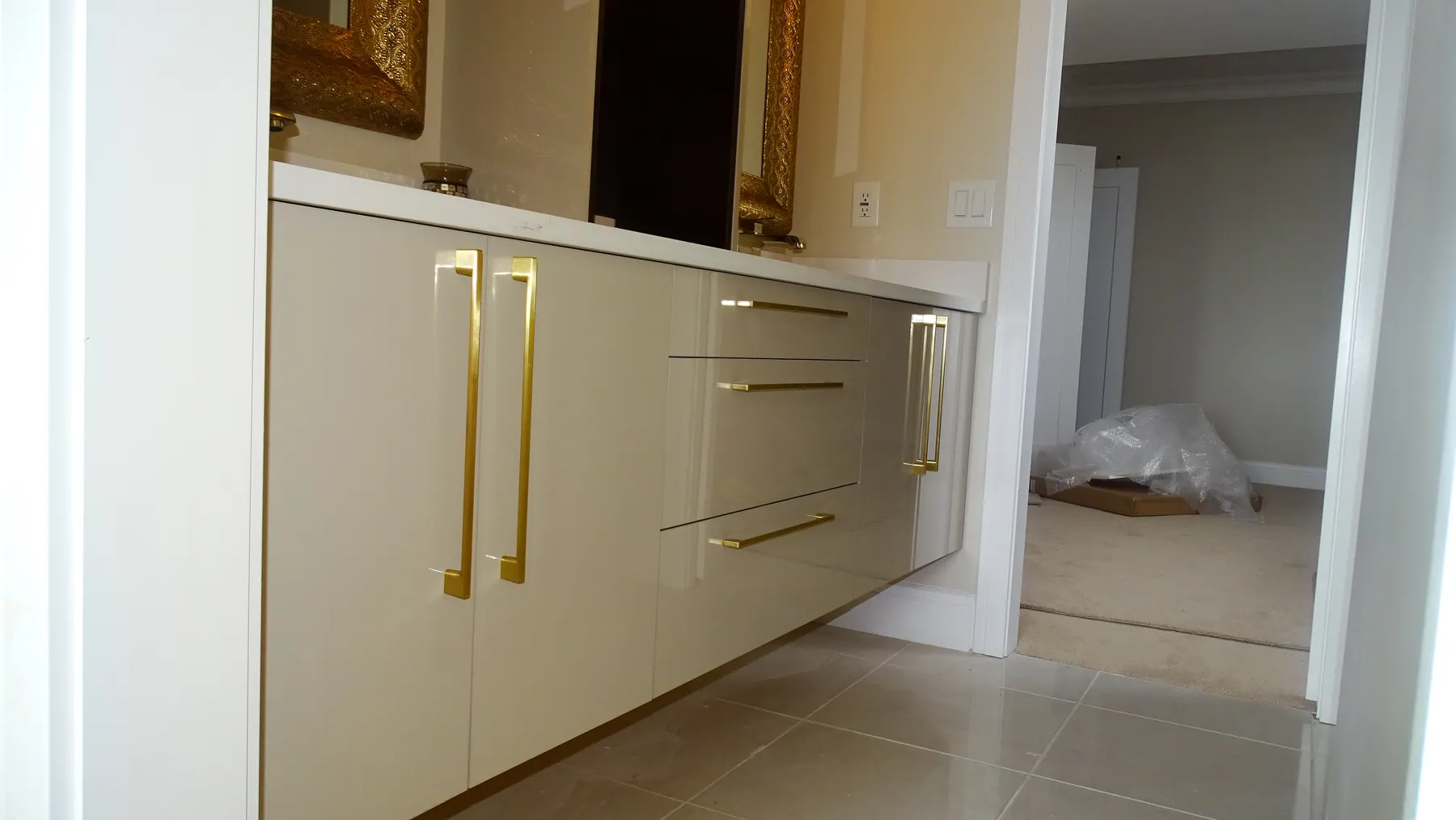 Gloss storage run with long brass bar pulls, beside a gold-framed mirror