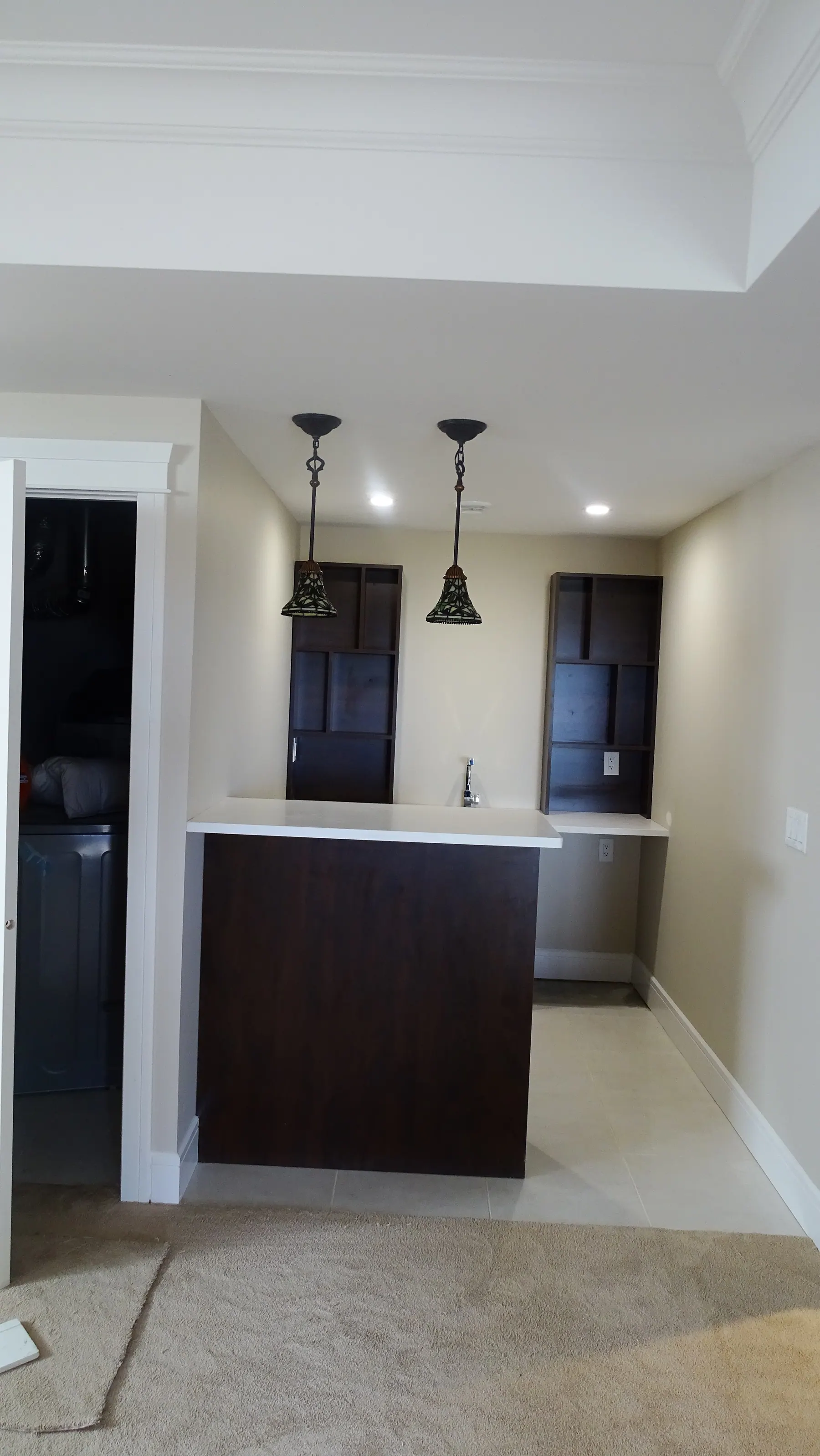 Bar counter in white quartz under two pendants, between espresso tall units
