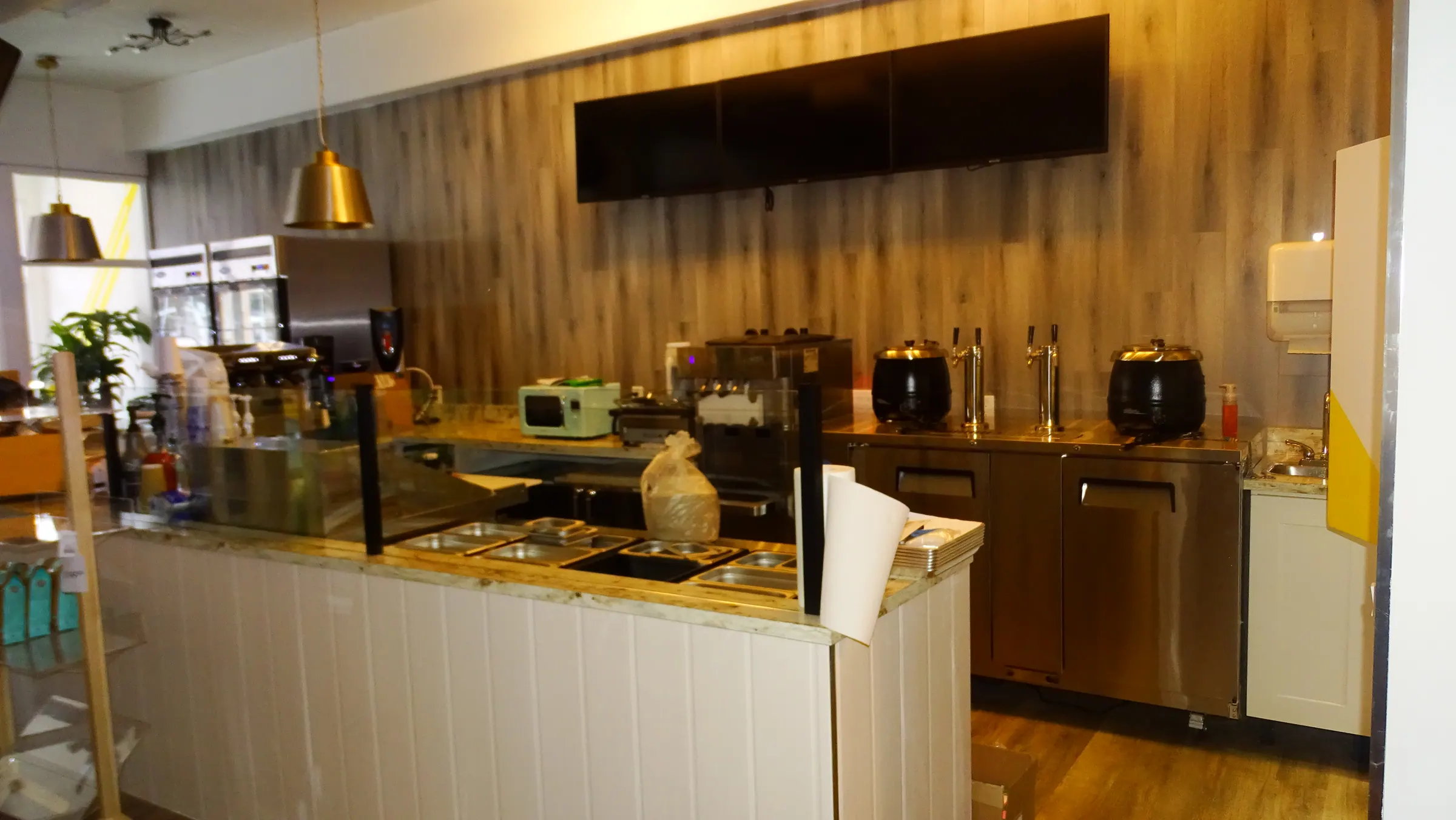 Restaurant interior with a white gloss service counter under a timber feature wall and a brass pendant